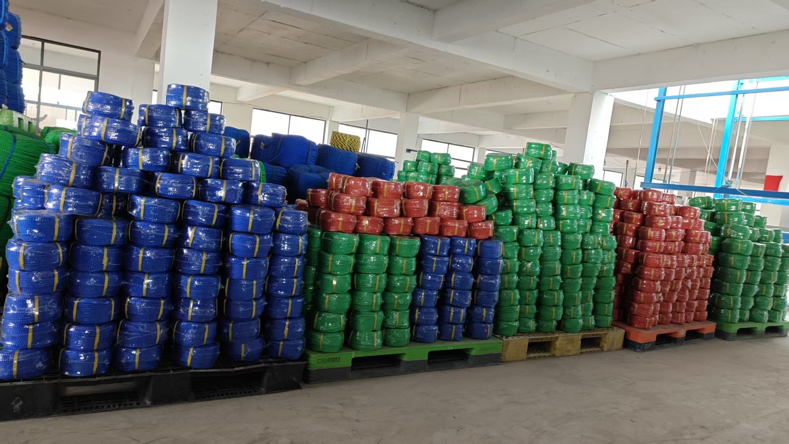 Warehouse pallets of 3-strand PE rope coils in blue, green, red and yellow, shrink-wrapped